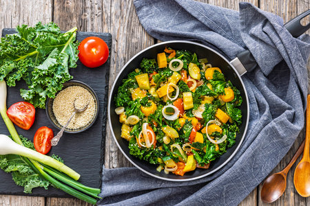 zucchini kale tomato saute sprinkled with sesame on a skillet on rustic wooden table with spoons and ingredients, horizontal view from above, flat layの写真素材