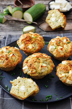 Savory Zucchini Feta Muffins on dark grey plate on rustic wood table with kitchen towel and ingredients, vertical view from above, not AI generated, close-upの写真素材