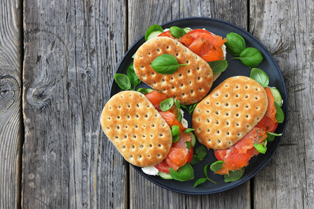 smoked salmon sandwiches with basil, cucumber, tomatoes and cream cheese on plate on rustic wood...