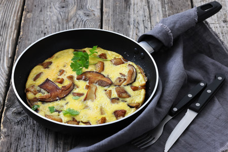 porcini mushroom parmesan omelette on a skillet on rustic wood table with cutlery, horizontal view from above, not AI generatedの写真素材