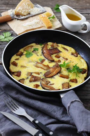 porcini mushroom parmesan omelette on a skillet on rustic wood table with cutlery and olive oil, vertical view from above, close-up, not AI generatedの写真素材