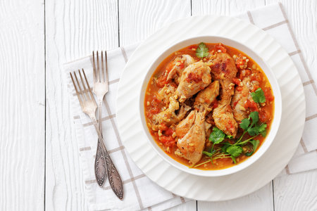 Chakhokhbili, Georgian chicken stew with tomato, herbs and chopped walnuts in a bowl on a white wood table with fresh cilantro, forks, horizontal view, fat lay, free space, not AI generatedの写真素材