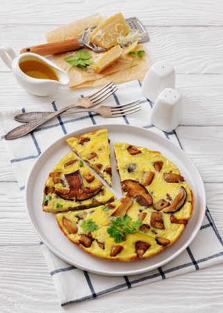 porcini mushroom parmesan omelette on a plate on white wood table with forks, olive oil, vertical view from aboveの写真素材