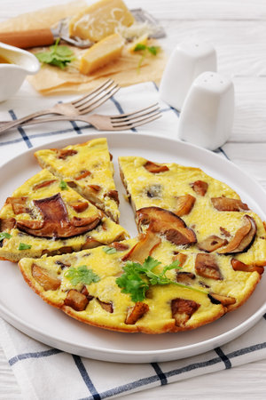 porcini mushroom parmesan omelette on a plate on white wood table with forks, olive oil, grated cheese, vertical view from above, close-up, not AI generatedの写真素材