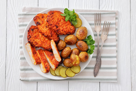 Paprika-Rubbed Pork Chops on a plate with cilantro, baked potatoes and sliced dill pickles on white wood table with forks and napkin, flat lay, close-up, not AI generatedの写真素材