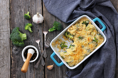 crunchy baked broccoli topped with panko breadcrumbs and parmesan in a baking dish on rustic wood table with forks and ingredients, horizontal view from above, flat lay, not AI generatedの写真素材