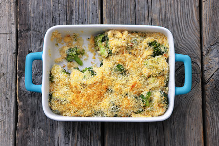 crunchy baked broccoli topped with panko breadcrumbs and parmesan cheese in a baking dish on rustic wood table, flat lay, close-up, not AI generatedの写真素材