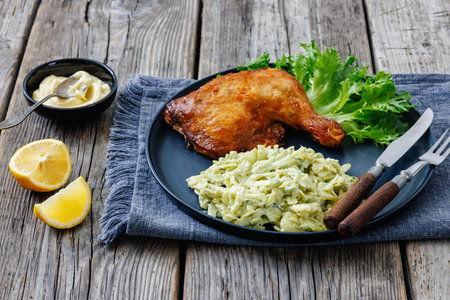roast chicken leg with cabbage artichoke salad on a plate with cutlery on rustic wood table with lemon and mayonnaise, horizontal view from above, close-up, not AI generatedの写真素材