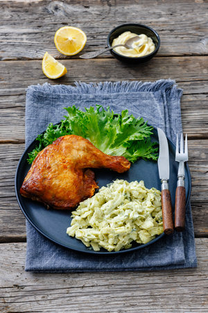 roast chicken leg with cabbage artichoke salad on a plate with cutlery on rustic wood table with lemon and mayonnaise, vertical view from above, close-up, not AI generatedの写真素材