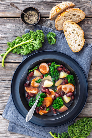 Red kidney bean, potato, kale and sausage soup in a black bowl with spoon on rustic wood table, vertical view from above, flat lay, not AI generatedの写真素材
