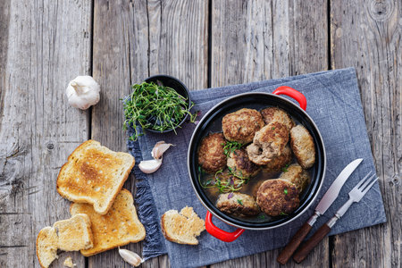 Frikadellen, Minced Meat Patties in red pot on rustic wood table with toasted bread, garlic, cutlery, horizontal view from above, flat lay, free space, not AI generatedの写真素材