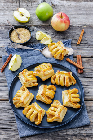 Puff Pastry Apple Pockets, Apple Hand Pies on plate on rustic wood table with fresh apples, cinnamon sticks and brown sugar, vertical view from aboveの写真素材