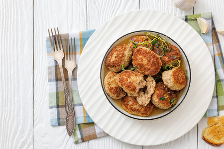 Frikadellen, Minced Meat Patties in white bowl on white wood table with napkin and forks, german...