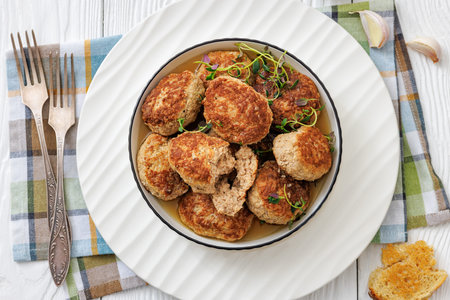 Frikadellen, Minced Meat Patties in white bowl on white wood table with napkin and forks, german...