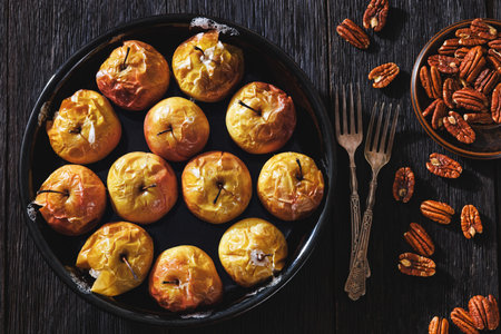 whole oven-baked apples in baking dish served with crunchy roasted pecans on a dark rustic wooden table with forks, flat lay, close-up,, not AI generatedの写真素材