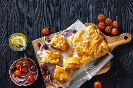 Bougatsa phyllo pastry with minced meat served on wooden cutting board with red onion, olives and...
