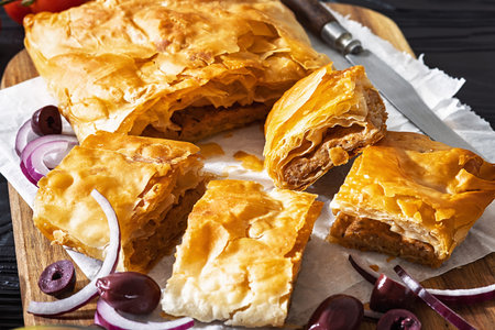 close-up of Sliced savory bougatsa phyllo pastry with minced meat served on wooden cutting board...