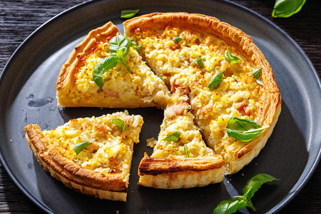 French Quiche Lorraine slices on a plate on dark wood table, horizontal view from above, close-up