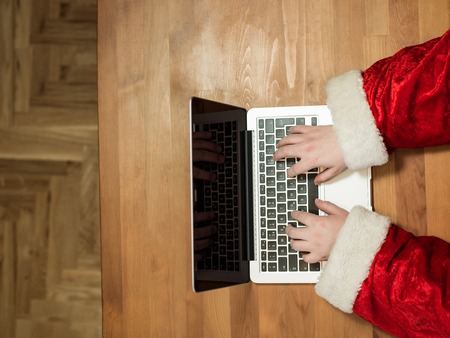Santa working at desk and typing on a laptop, Christmas gifts and letters, hands top viewの写真素材