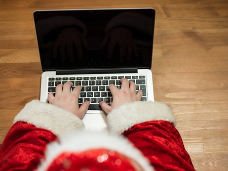 Santa working at desk and typing on a laptop, Christmas gifts and letters, hands top viewの写真素材
