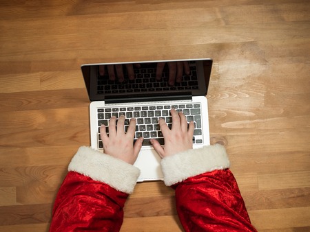Santa working at desk and typing on a laptop, Christmas gifts and letters, hands top viewの写真素材