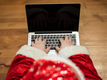 Santa working at desk and typing on a laptop, Christmas gifts and letters, hands top viewの写真素材