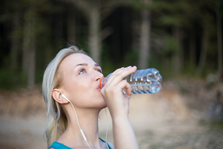 Woman fitness runner drinking and splashing water in her face. Funny image of beautiful female fitness modelの写真素材