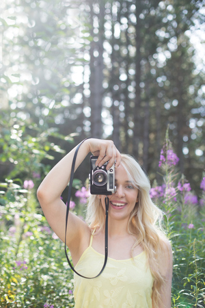 Outdoor summer smiling lifestyle portrait of pretty young blonde woman having fun in the nature, camera travel photo of photographer Making pictures in hipster styleの写真素材