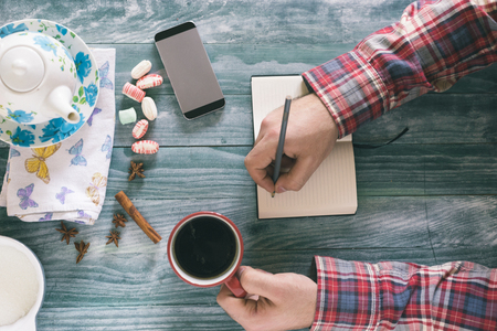 Man reading a book on wooden table with coffee, notes and smart phone.の写真素材