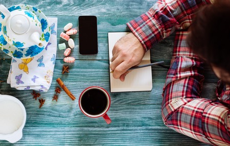 Man reading a book on wooden table with coffee, notes and smart phone.の写真素材