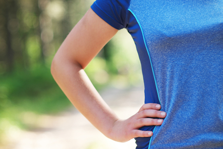 Cropped shot of fit woman in sports wear standing with her hand on hip outdoors, with sun flare.の写真素材