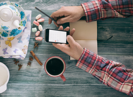 Man reading a book on wooden table with coffee, notes and smart phone.の写真素材