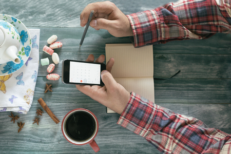 Man reading a book on wooden table with coffee, notes and smart phone.の写真素材
