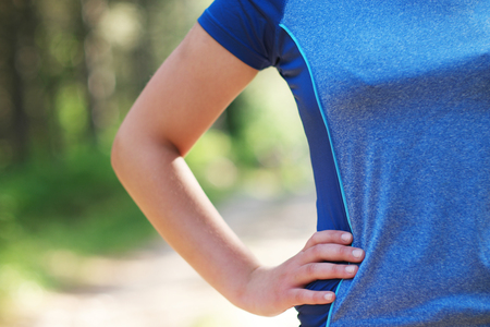 Cropped shot of fit woman in sports wear standing with her hand on hip outdoors, with sun flare.の写真素材