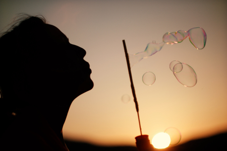 Happy blowing bubbles in the park at sunset.の写真素材