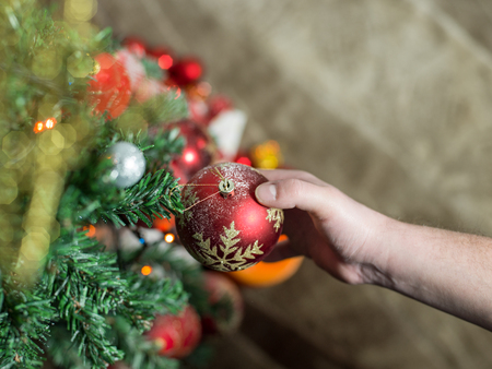 Close-up of man hanging decorative toy ball on Christmas tree branchの写真素材