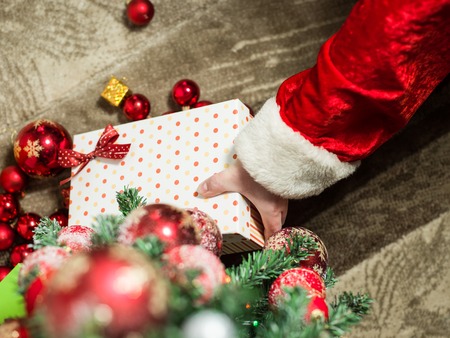 holidays, celebration and people concept - close up of santa claus putting present under christmas treeの写真素材