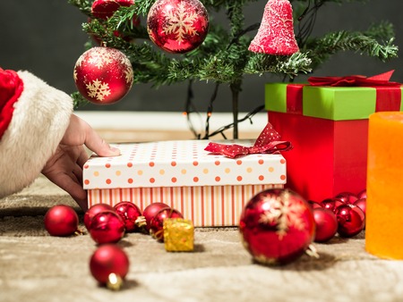 holidays, celebration and people concept - close up of santa claus putting present under christmas treeの写真素材
