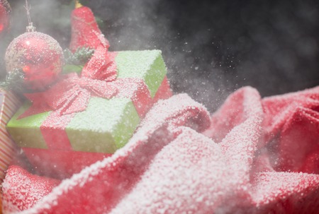green Christmas gift box with its lid propped at an angle in front to display the beautiful red  ribbon with falling winter snowflakes and copyspace for your greeting or wishesの写真素材