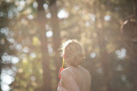 Gorgeous young brunette girl blowing soap bubbles in sunlit park.の写真素材