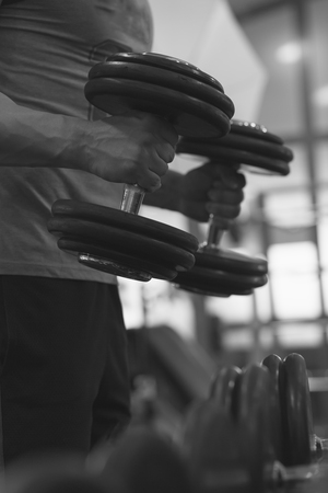 Closeup of a muscular young man lifting weights on dark backgroundの写真素材