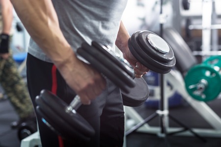 Muscular Young Man Doing Heavy Weight Exercise For Biceps With Dumbbells In Modern Fitness Centerの写真素材