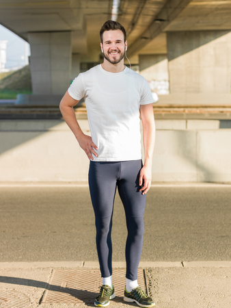 Young handsome man running along the embankment near the river under the bridgeの写真素材