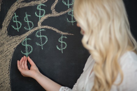 Happy blonde Business woman picking money off of a money tree, chalkboardの写真素材