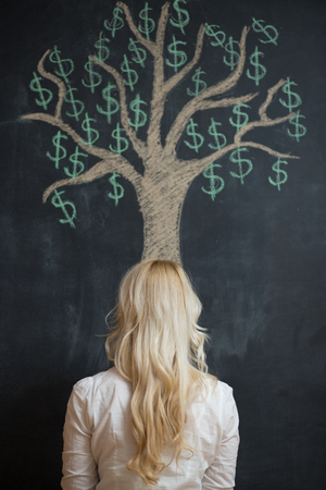 Happy blonde Business woman in front of chalk money tree drawing on blackboard.の写真素材