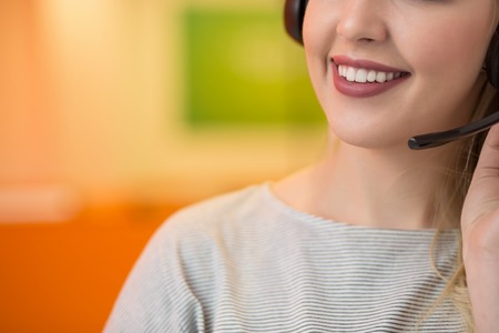 Close up of a blonde smiling woman wearing headset in her officeの写真素材