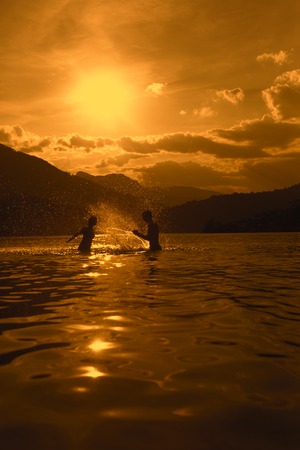 Silhoueted young couple at the beach on a hazy summer day at dusk,  enjoying splashing in the ocean water, getting wet,の写真素材