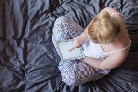 Young woman using tablet pc sitting on the bed. Relaxed internet searching on line shopping. top view.の写真素材