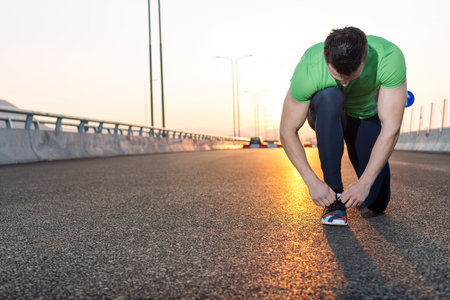Urban jogger tying his running shoes on a big bridge. sunset highway