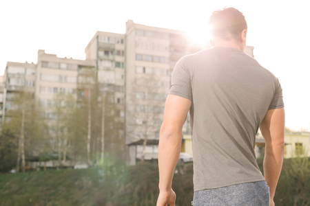 portrait of male runner resting after workout outdoors while enjoying beautiful sunrise in summer morning, handsome athletic man taking break after run outside in park while looking awayの写真素材